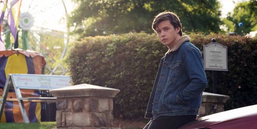 Nick Robinson as Simon leaning against a car near a state fair in Love, Simon