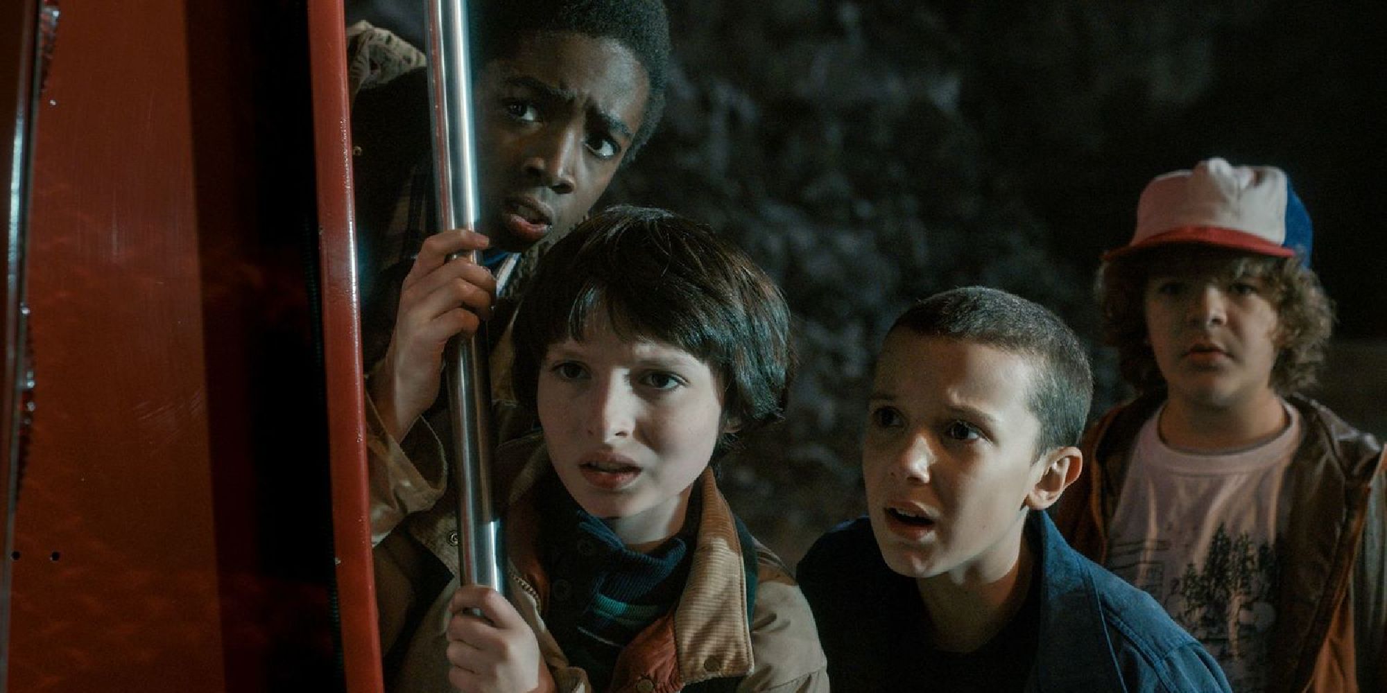 Lucas, Mike, Eleven, and Dustin hide behind a truck at the end of Season 1, Episode 3