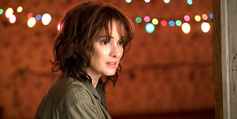 A disheveled Joyce at her front door with Christmas lights hung behind her