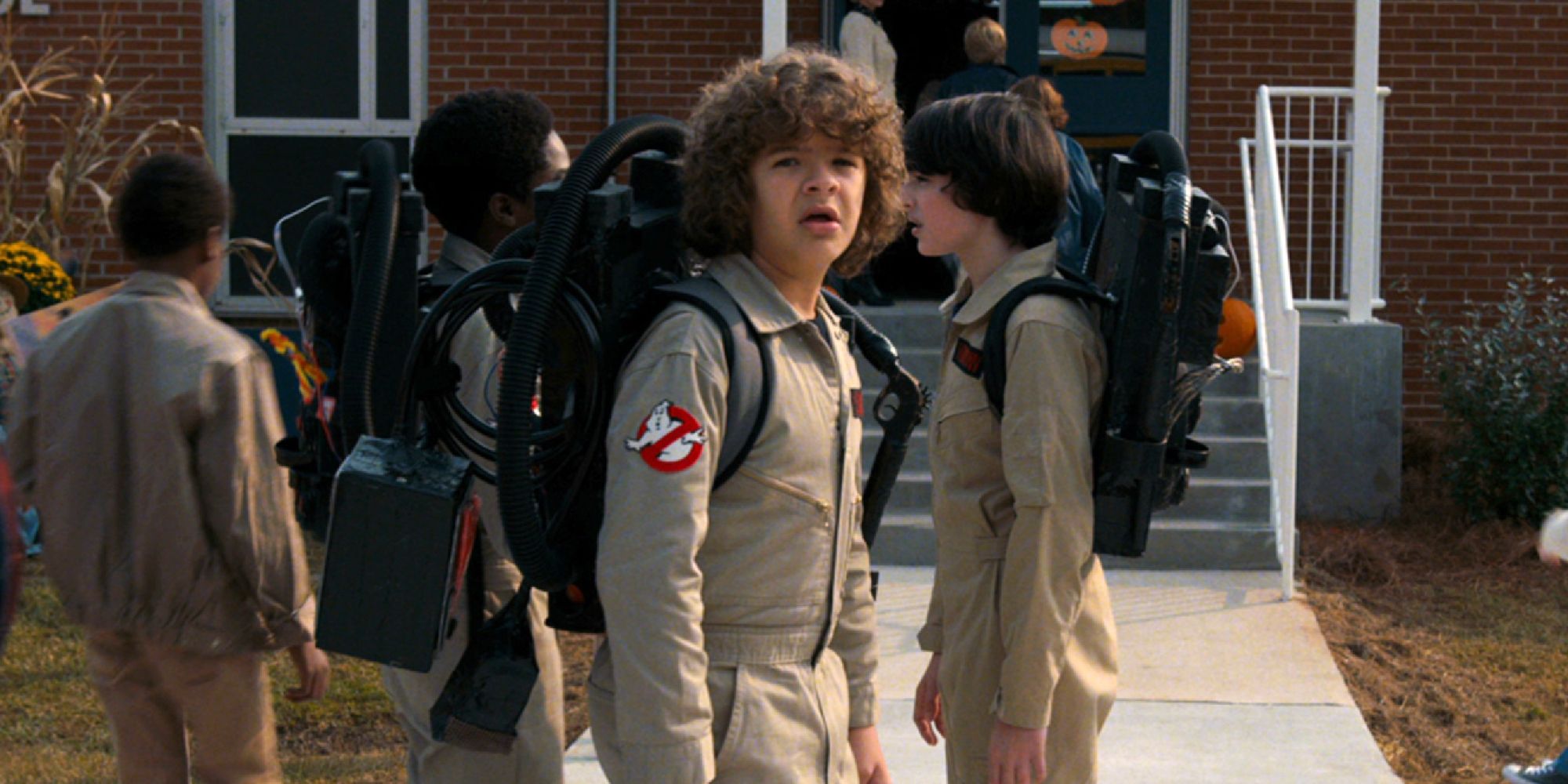 Dustin standing in front of Mike and Lucas, all dressed as Ghostbusters