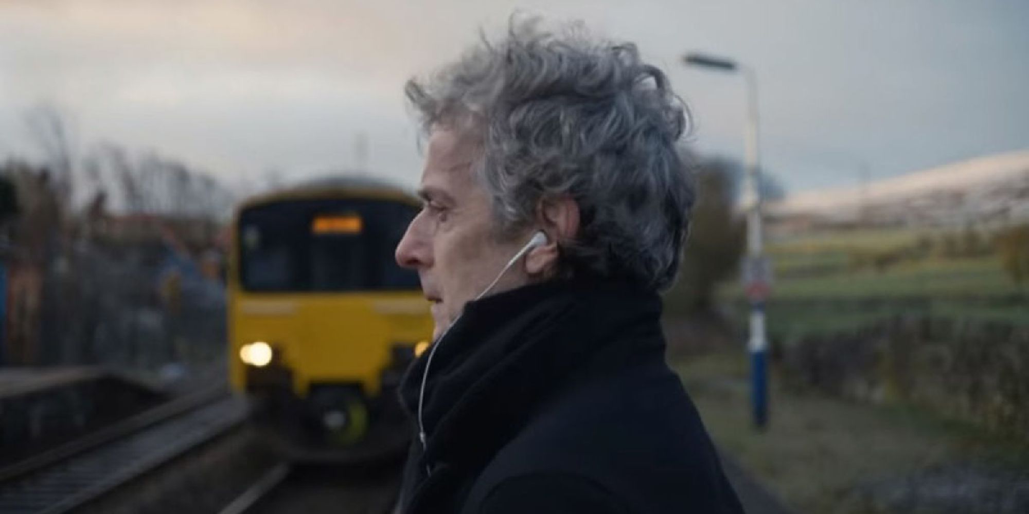Peter Capaldi waiting for a train with earbuds in the Someone You Loved video
