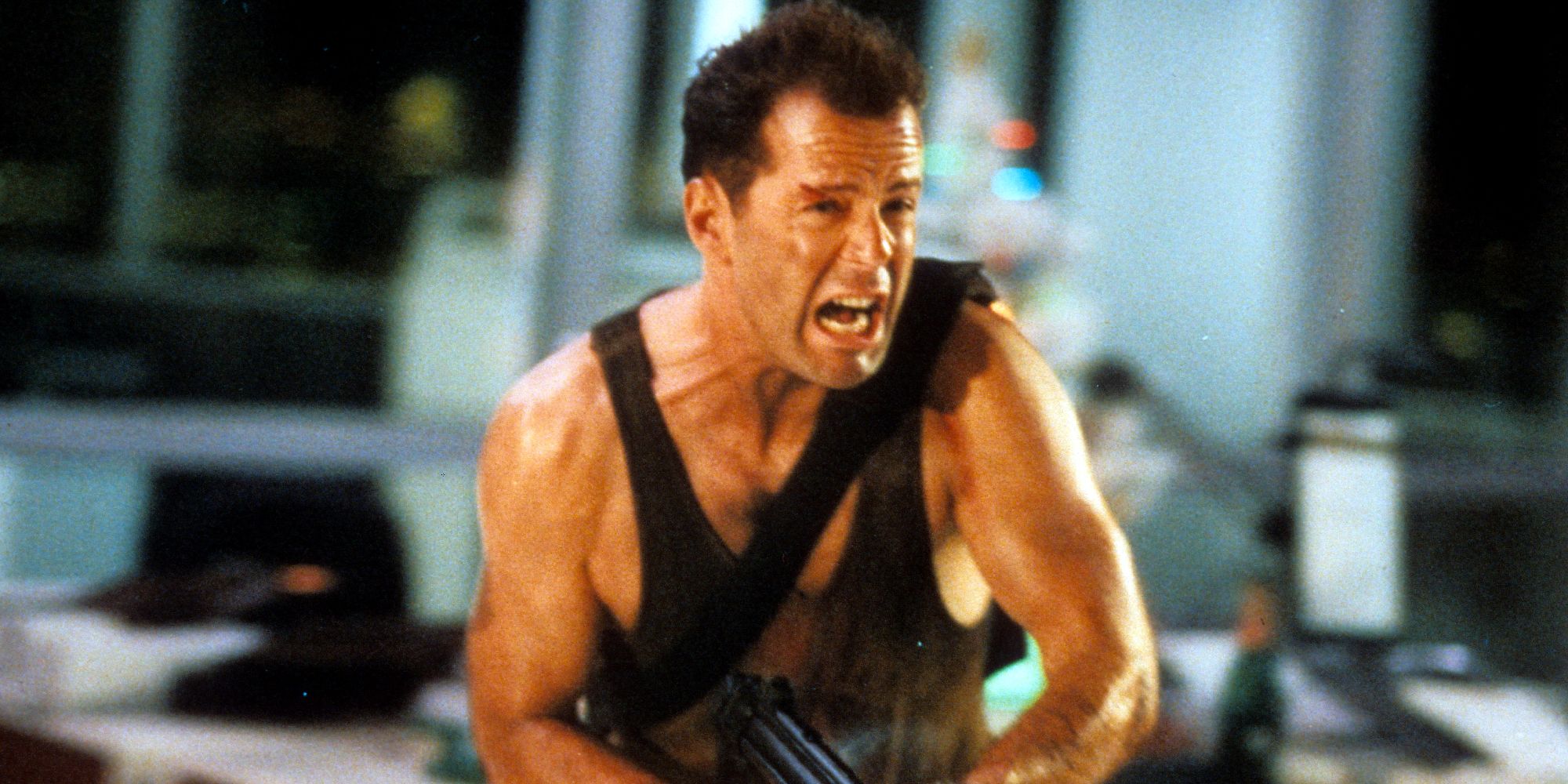 Bruce Willis running through an office with a gun as John McClane in Die Hard
