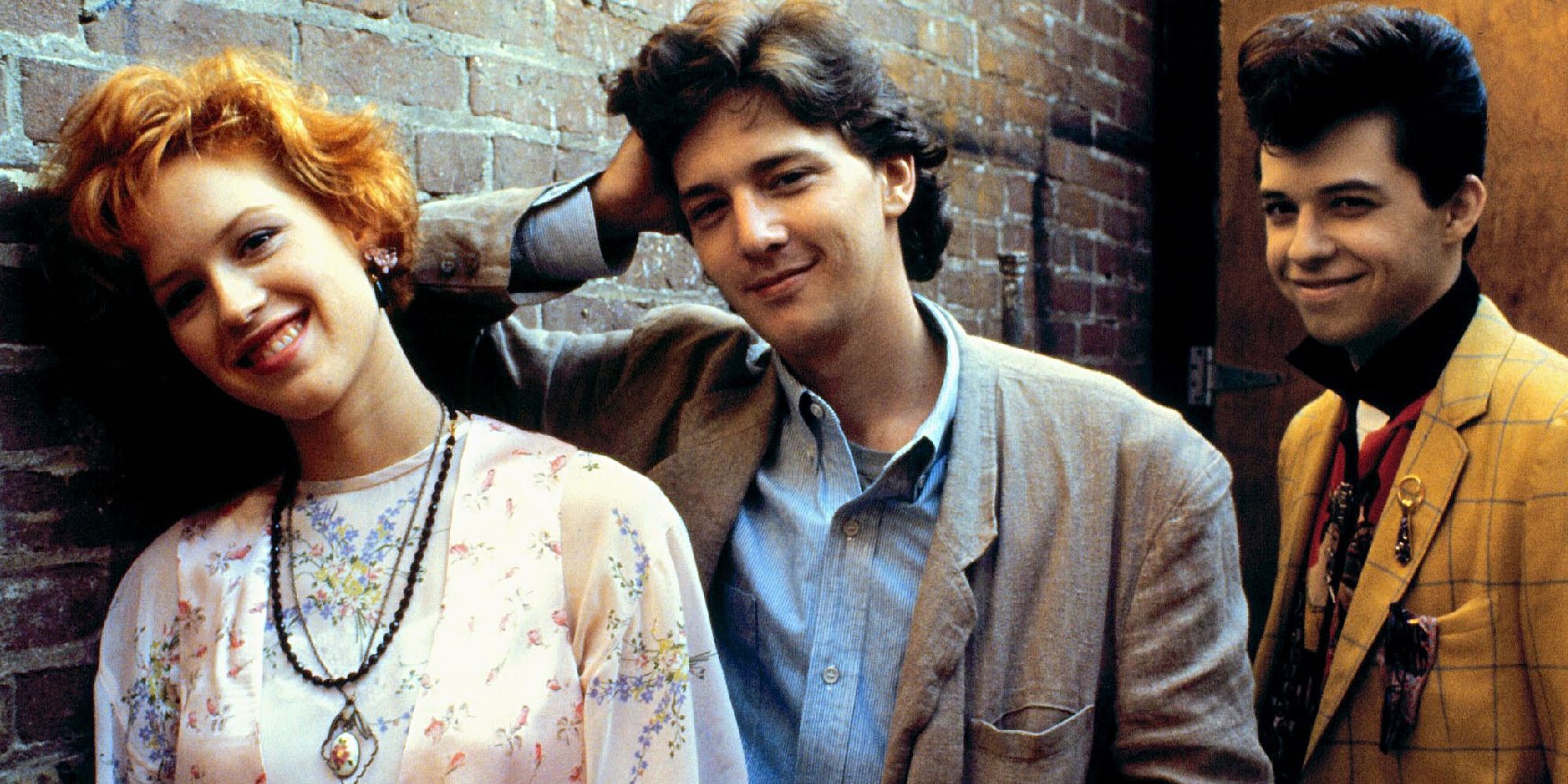 Molly Ringwald, Andrew McCarthy, and Jon Cryer against a brick wall in a promo pic for Pretty in Pink