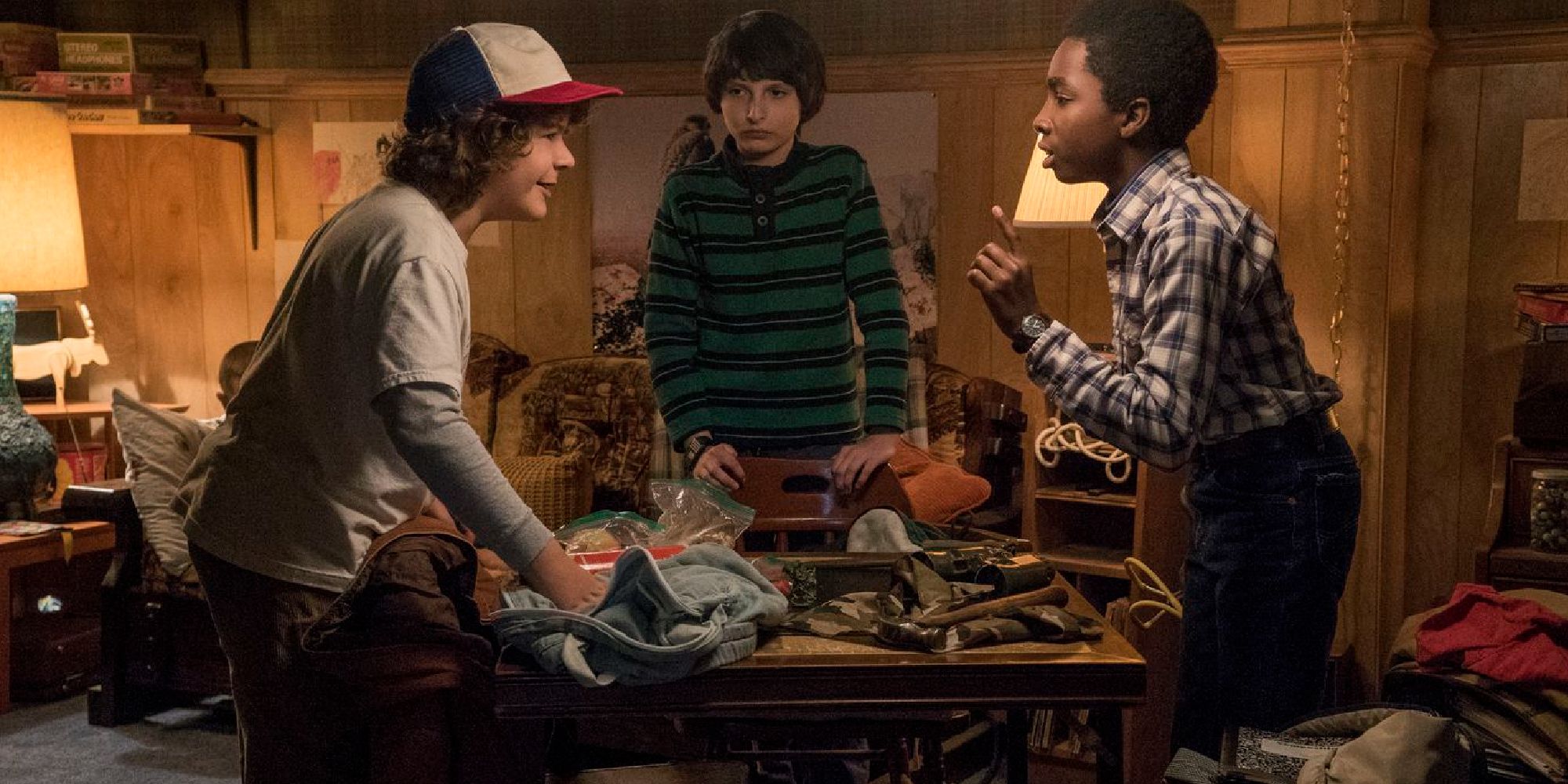 Mike, Dustin, and Lucas arguing around a table in Mike's basement in season 1 of Stranger Things