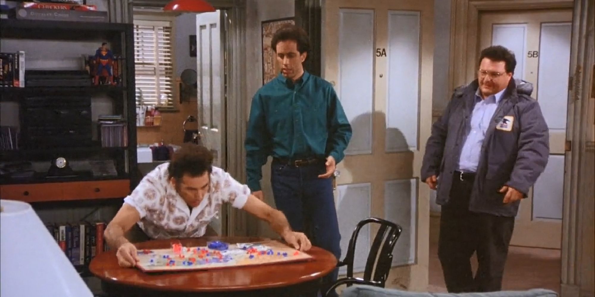 Kramer placing a game of Risk on a table in Jerry's apartment while Newman watches