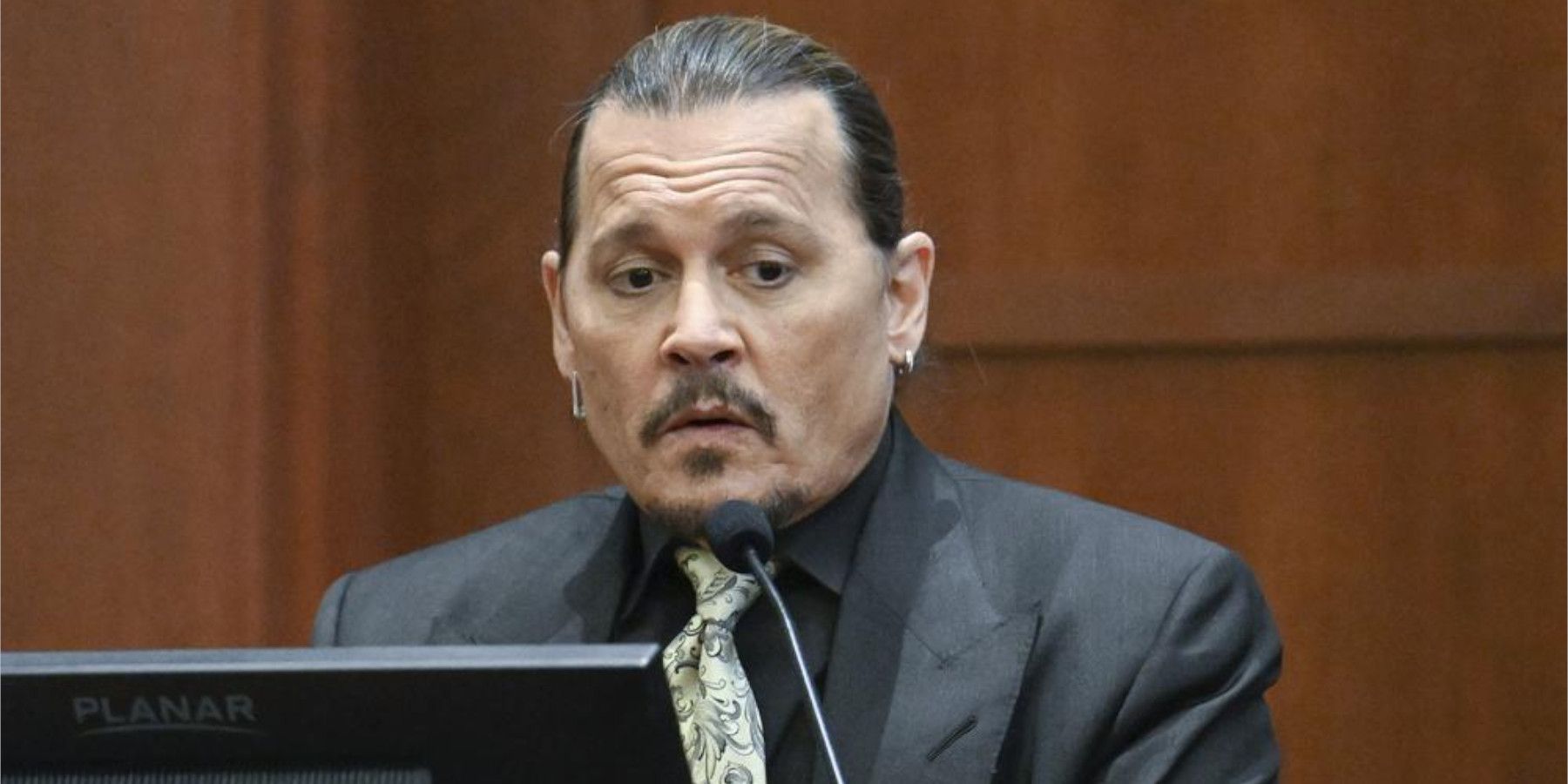 Johnny Depp, a famous actor, appears in a suit behind a court room microphone.