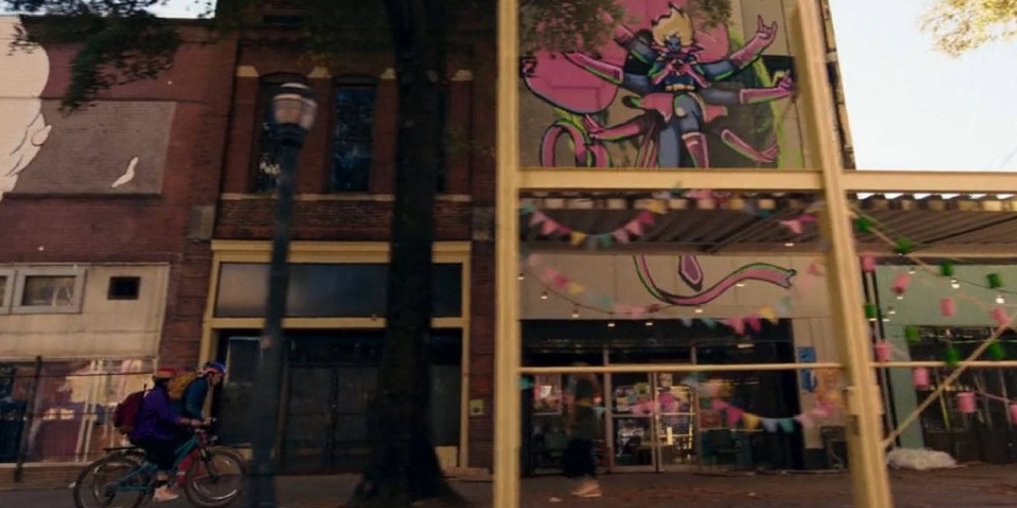 Bruno and Kamala biking beside a building with animated art depicting a Captain Marvel/Doctor Strange crossover