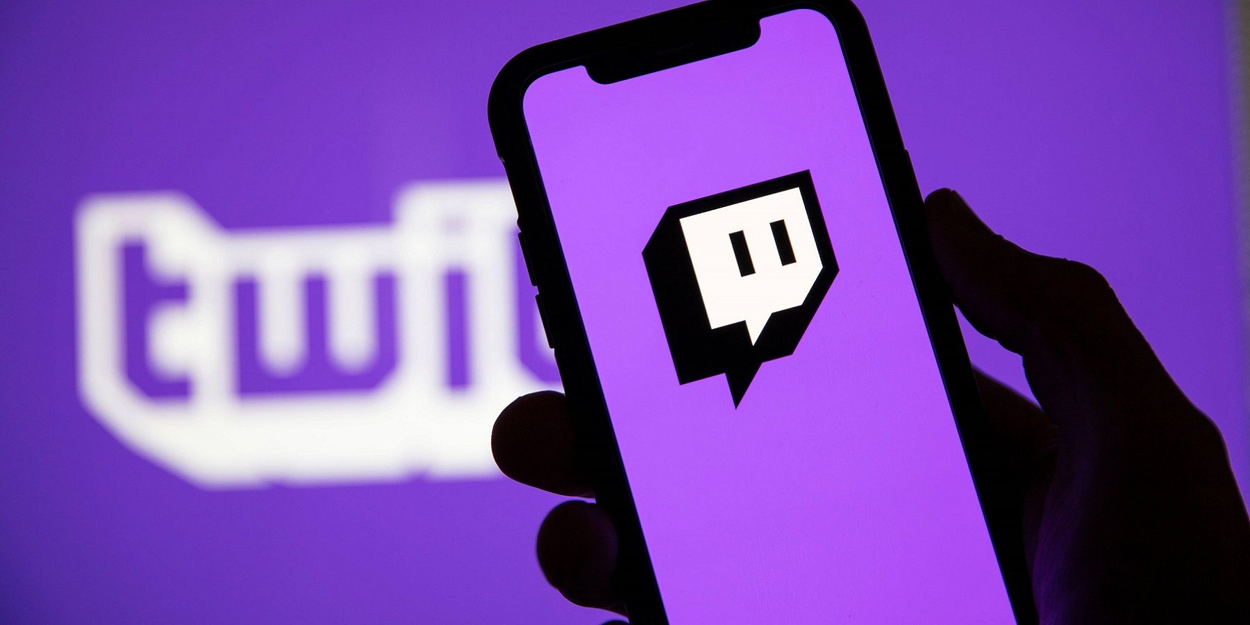 A han holding a phone that has the twitch logo on the screen, all on a purple background.