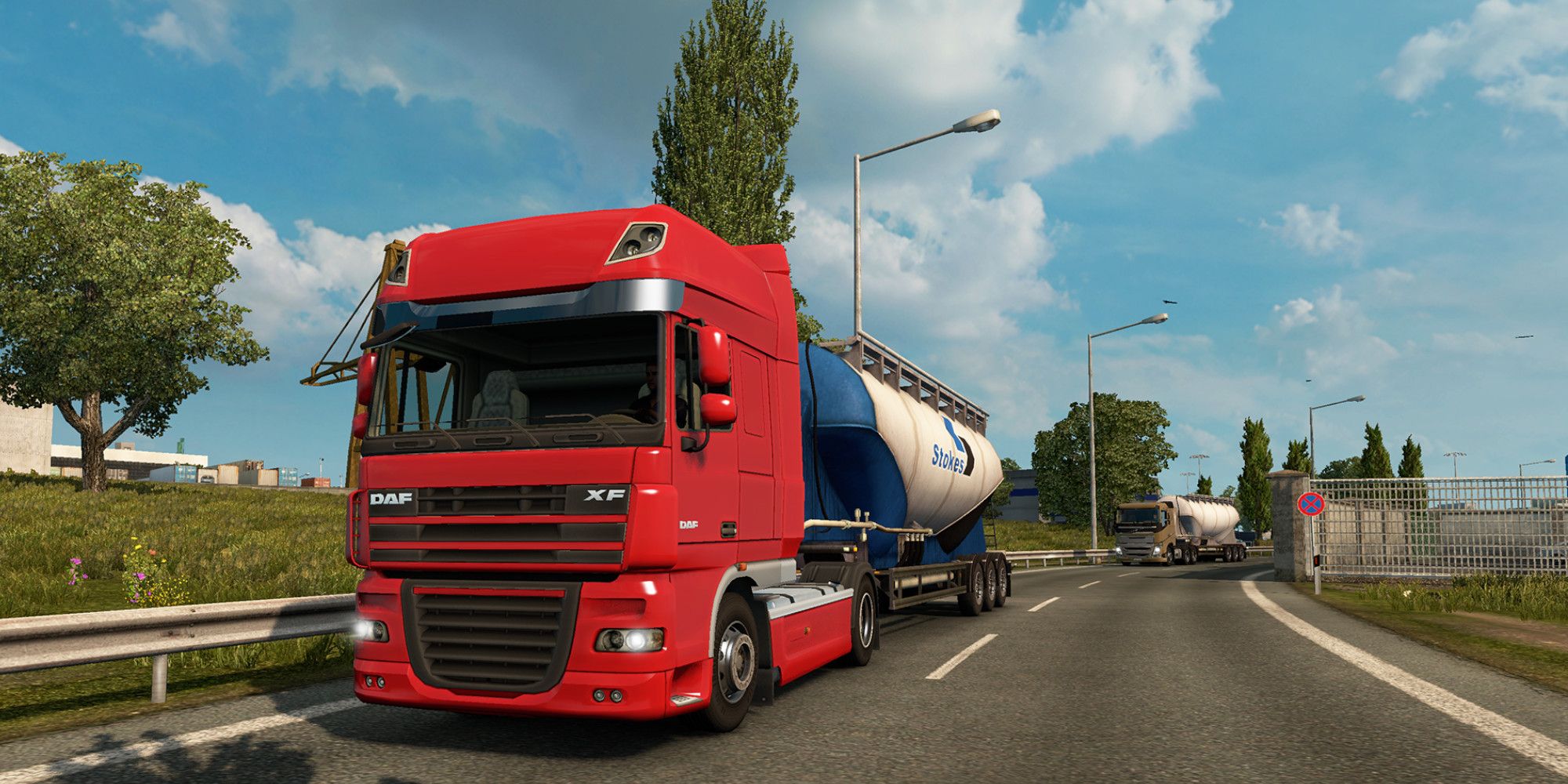 A red truck pulls a gas tanker trailer along an urban road