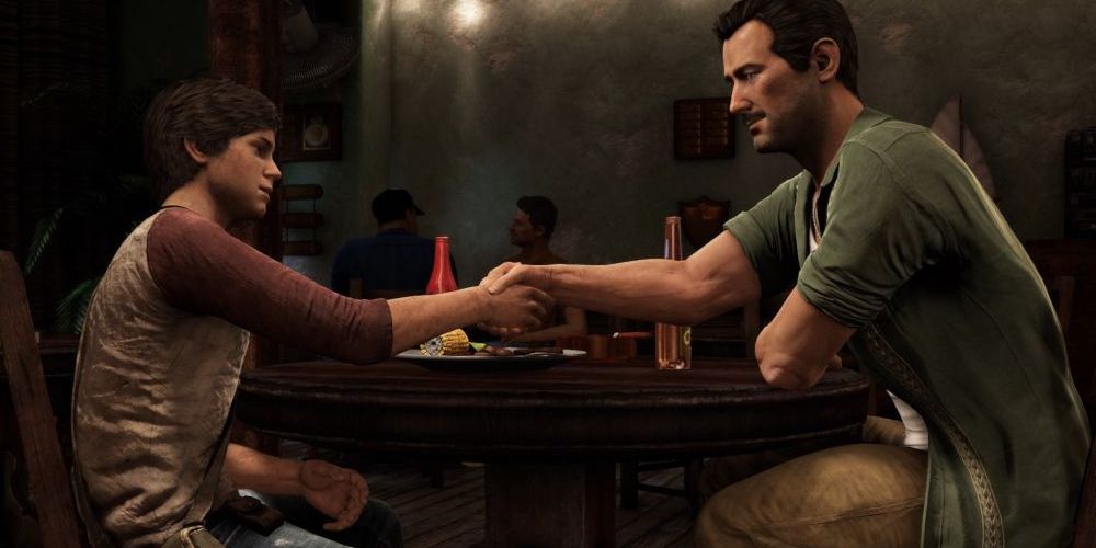 A young Nathan Drake (left) shakes hands with Sully (right) over a table at a dimly lit restaurant. Image source: Game Rant