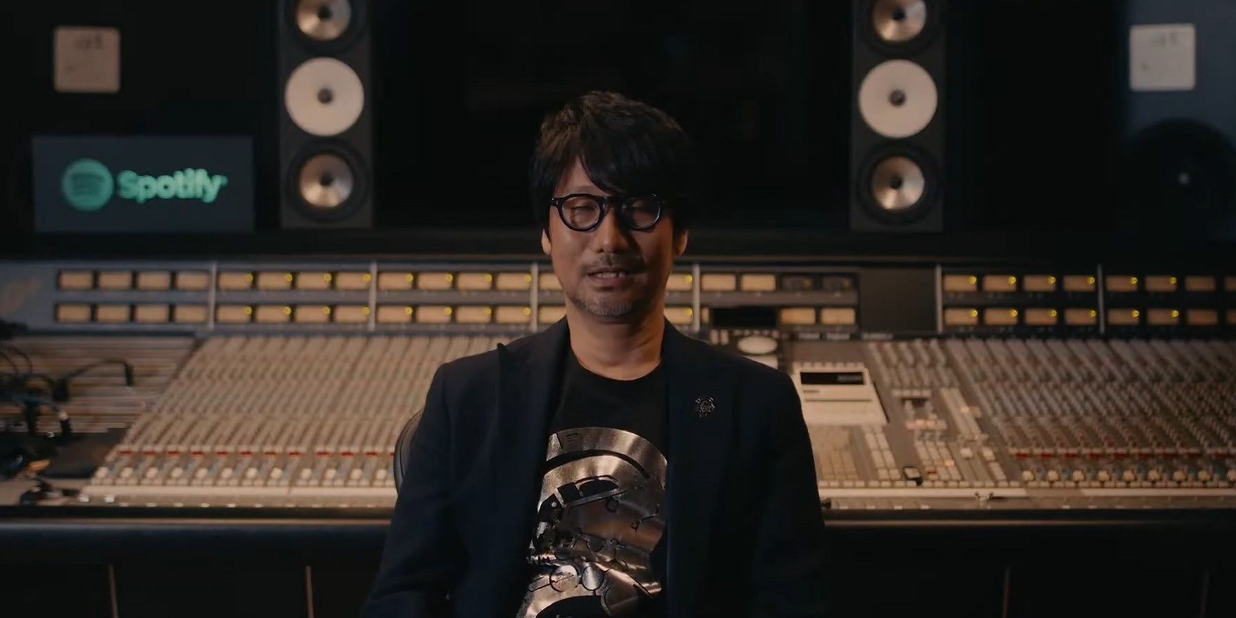 An image of Hideo Kojima sat in front of a studio mixing desk.