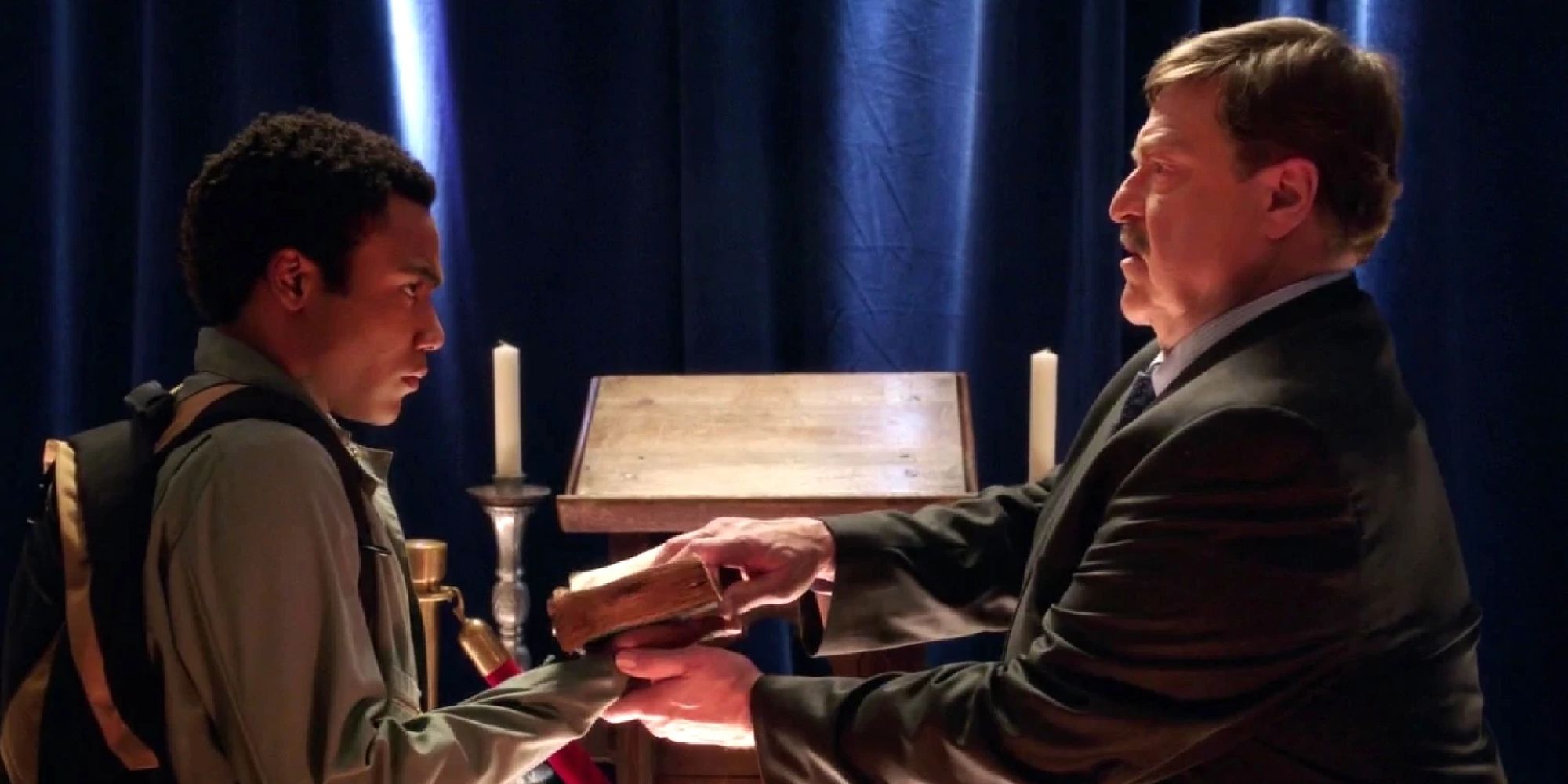 Vice Dean Laybourne handing Troy an ancient book in season 3