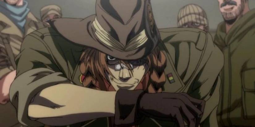 A brown haired man in a militaristic uniform sat on a backwards chair and surrounded by other similarly dressed men