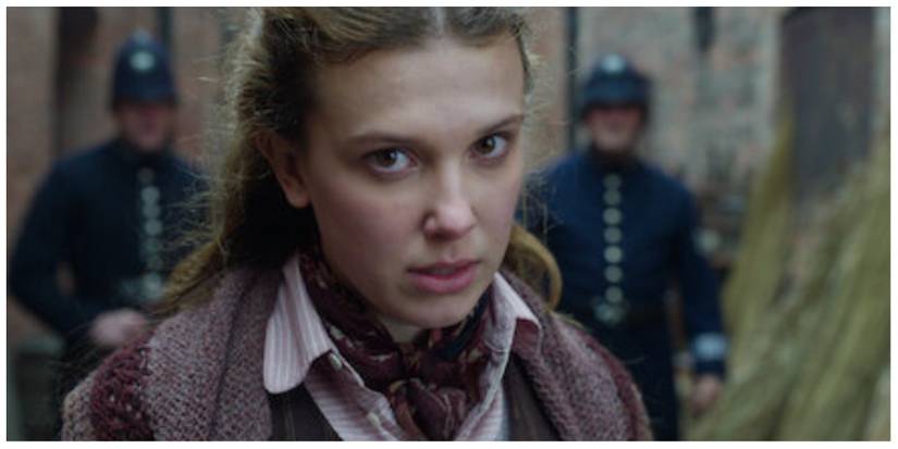 Enola Holmes looking directly at the camera with an angry look in her eye as she tries to evade police