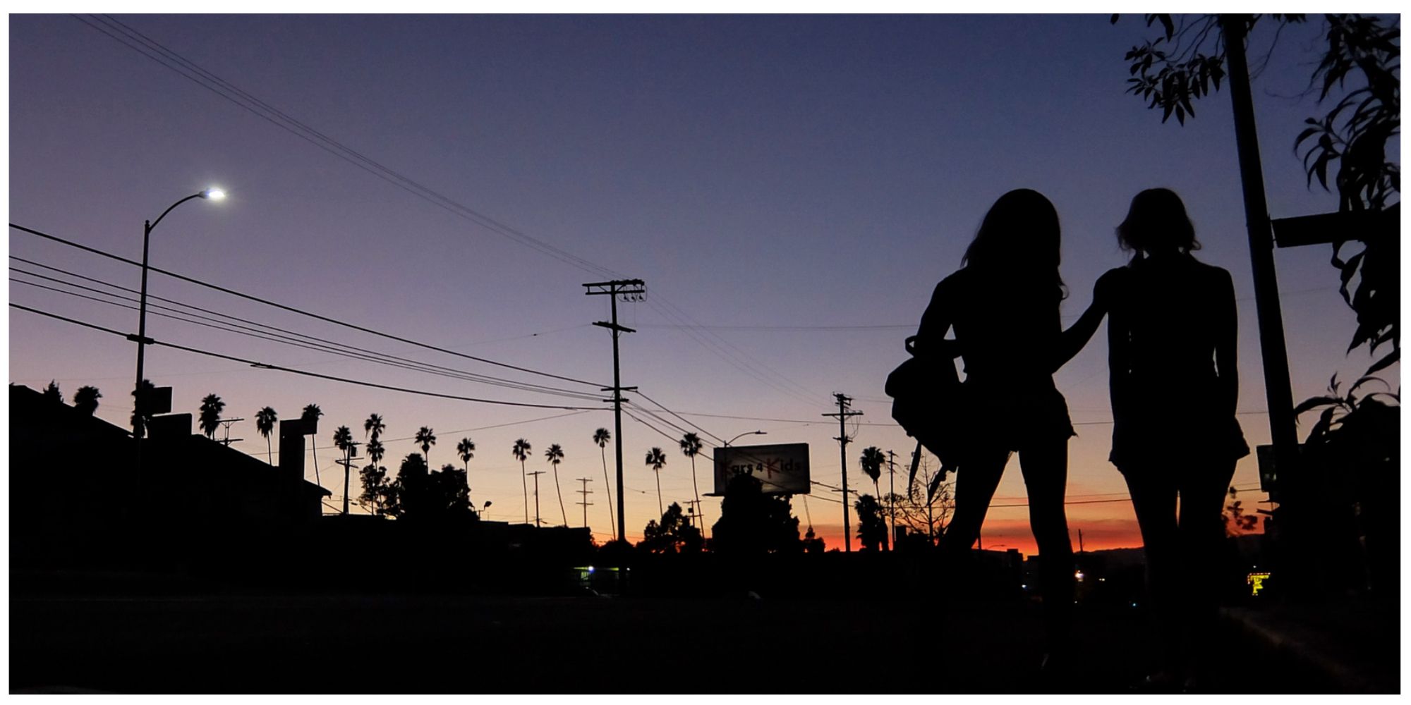 The silhouette of Sin-Dee and Alexandra standing on the street looking at the sunset