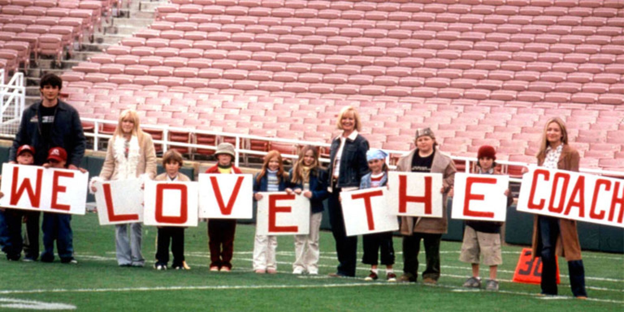 The Baker Children on a football pitch holding up signs saying 'We Love the Coach'