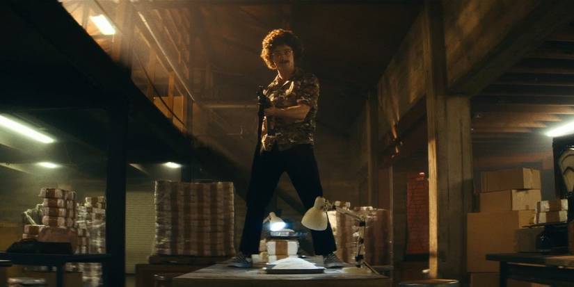 Daniel Radcliffe as Weird Al Yankovic firing machine gun on table