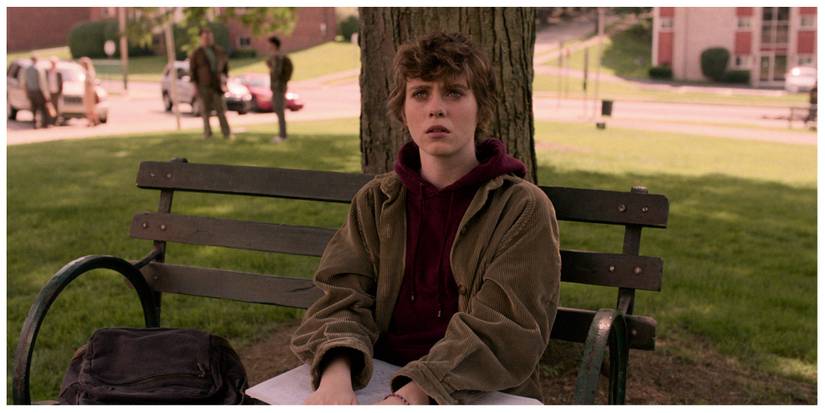 Sydney from the show sat on a bench at school looking confused and a bit nervous