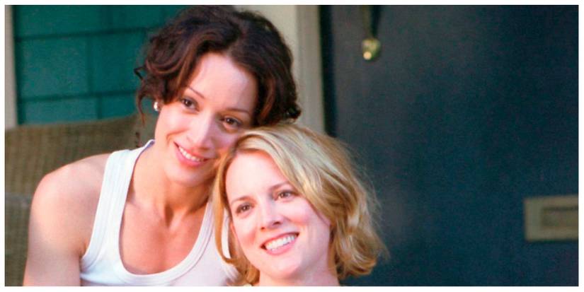 Bette and Tina from The L Word leaning against each other on their front porch and smiling at their friends