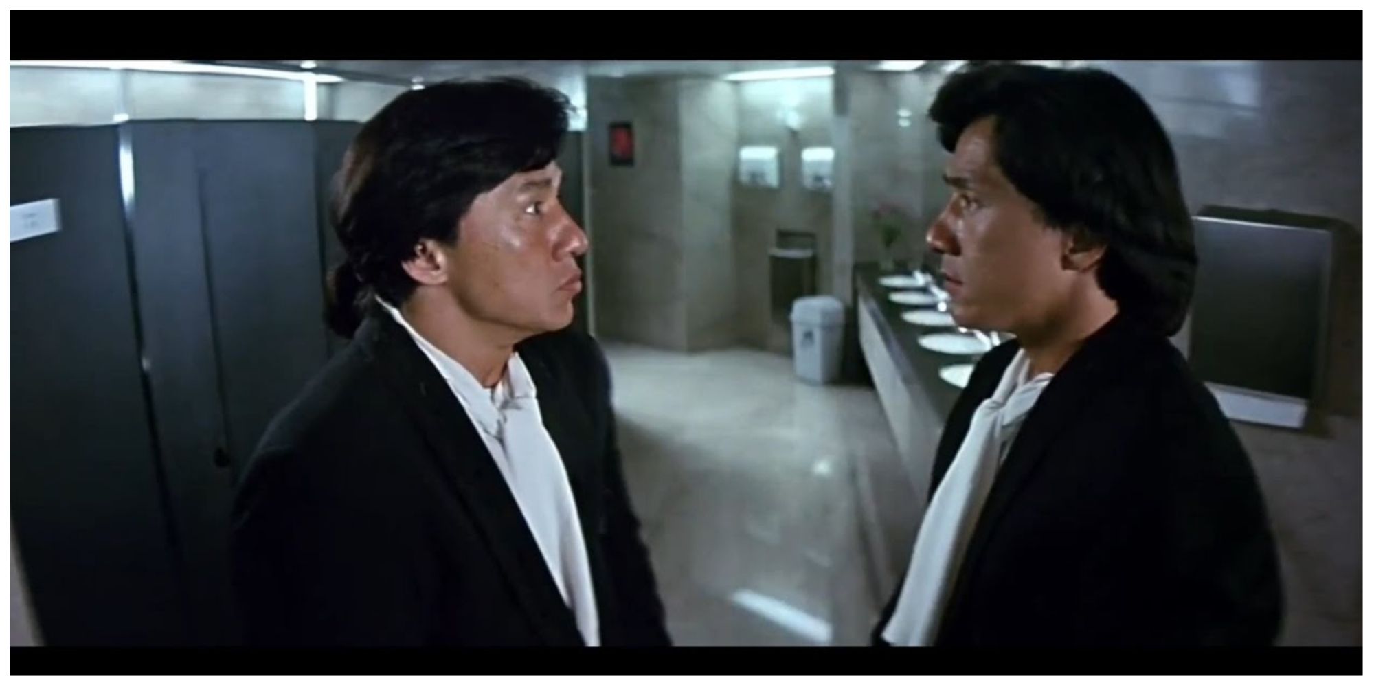 Jackie Chan starring as both twins in Twin Dragons. They are standing in a public bathroom staring at each other in shock.