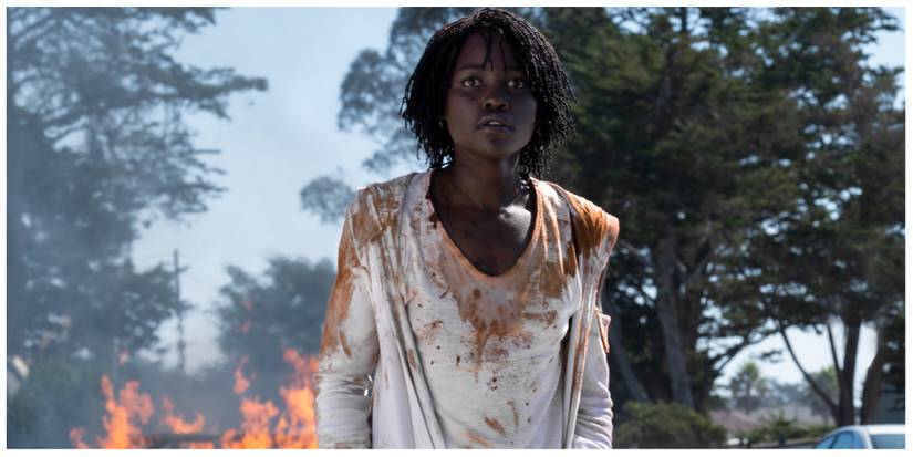 Lupita Nyong'o in Us looking scared at something off screen with a fire in the background