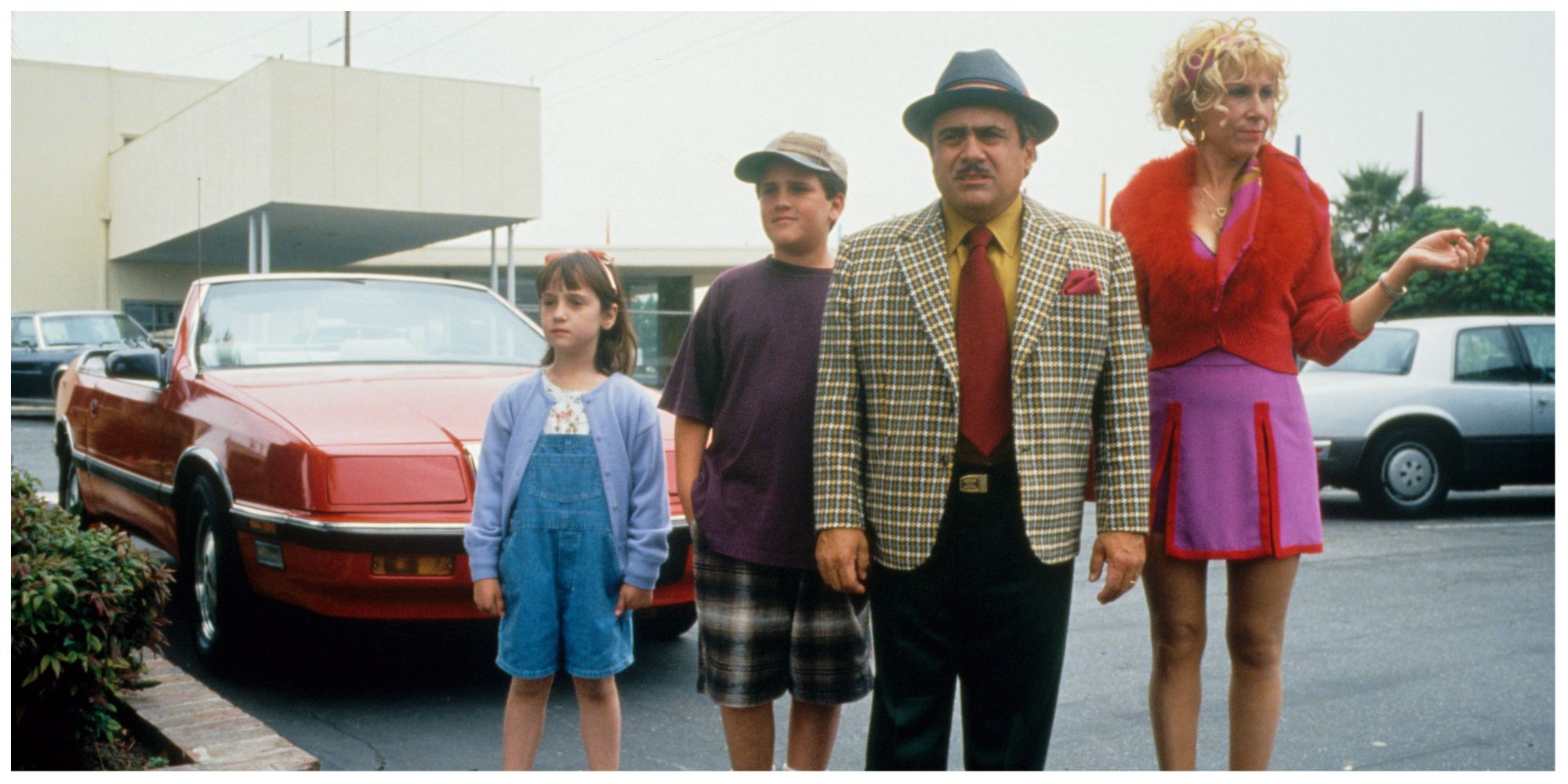 The Wormwood family in Matilda stood in a car park staring at something offscreen