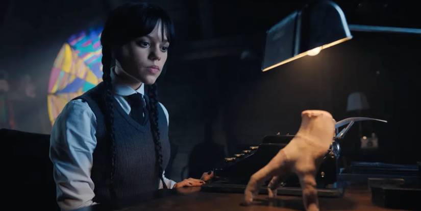 Wednesday Addams sitting at her desk with her typewriter and Thing