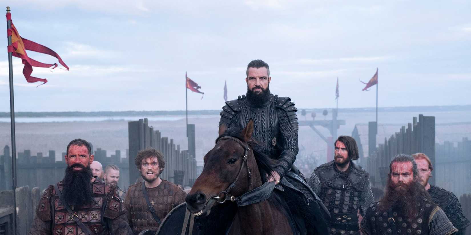 Canute in armour riding a horse surrounded by warriors