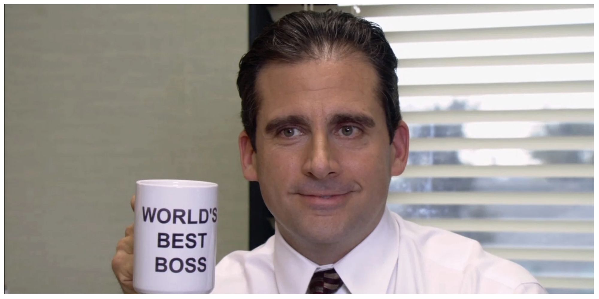 Michael Scott holding up his infamous 'World's Best Boss' mug with a smile