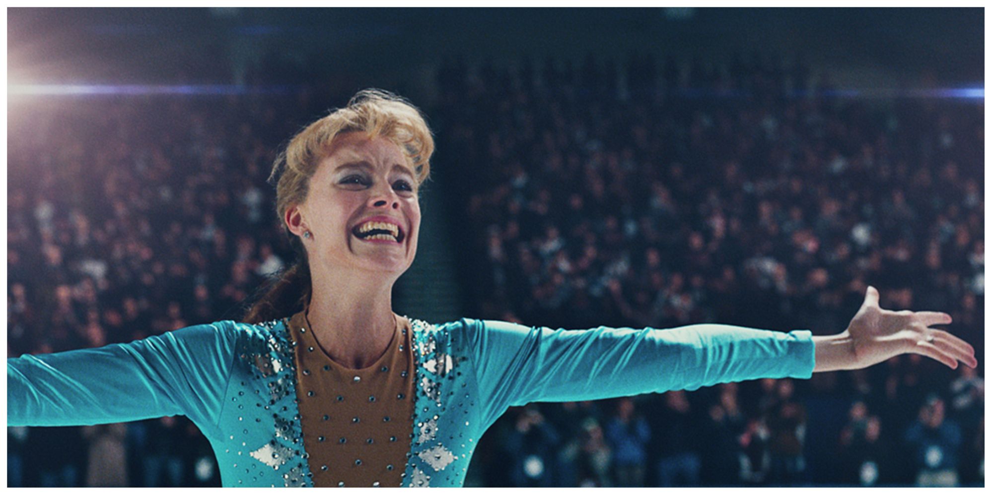 Margot Robbie as Tonya on the ice rink holding her arms up in celebration to the crowd