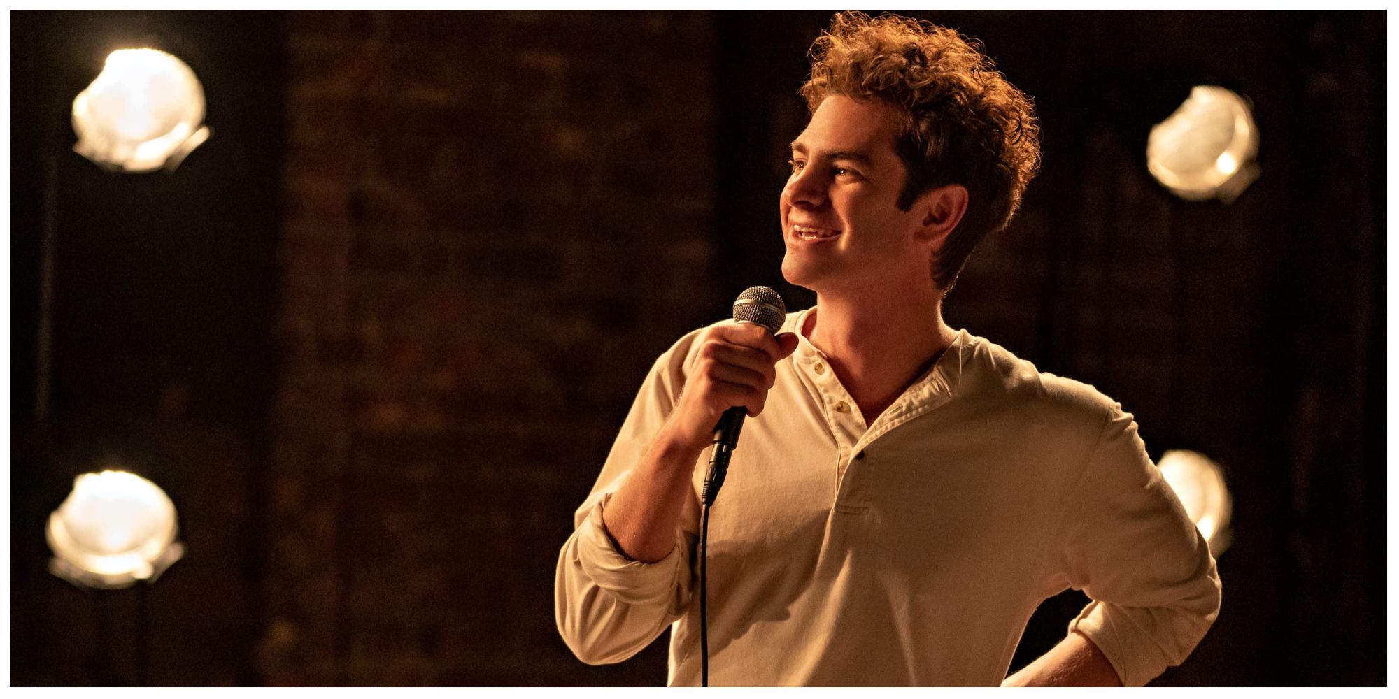 Andrew Garfield in Tick Tick Boom smiling on stage with a microphone