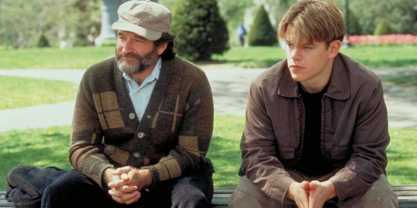Sean McGuire and Will Hunting sit side by side on a park bench. Sean is smiling while Will looks pensive,