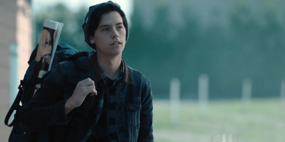 Riverdale Jughead with a backpack and poster walking past a field