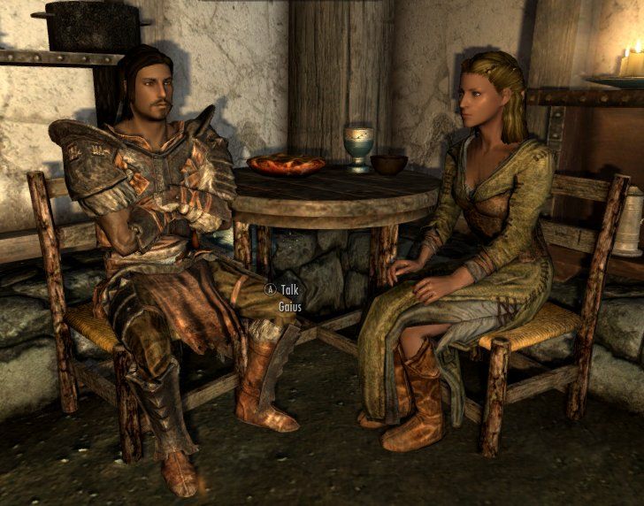 Screenshot from Skyrim showing two characters sitting at a table inside.