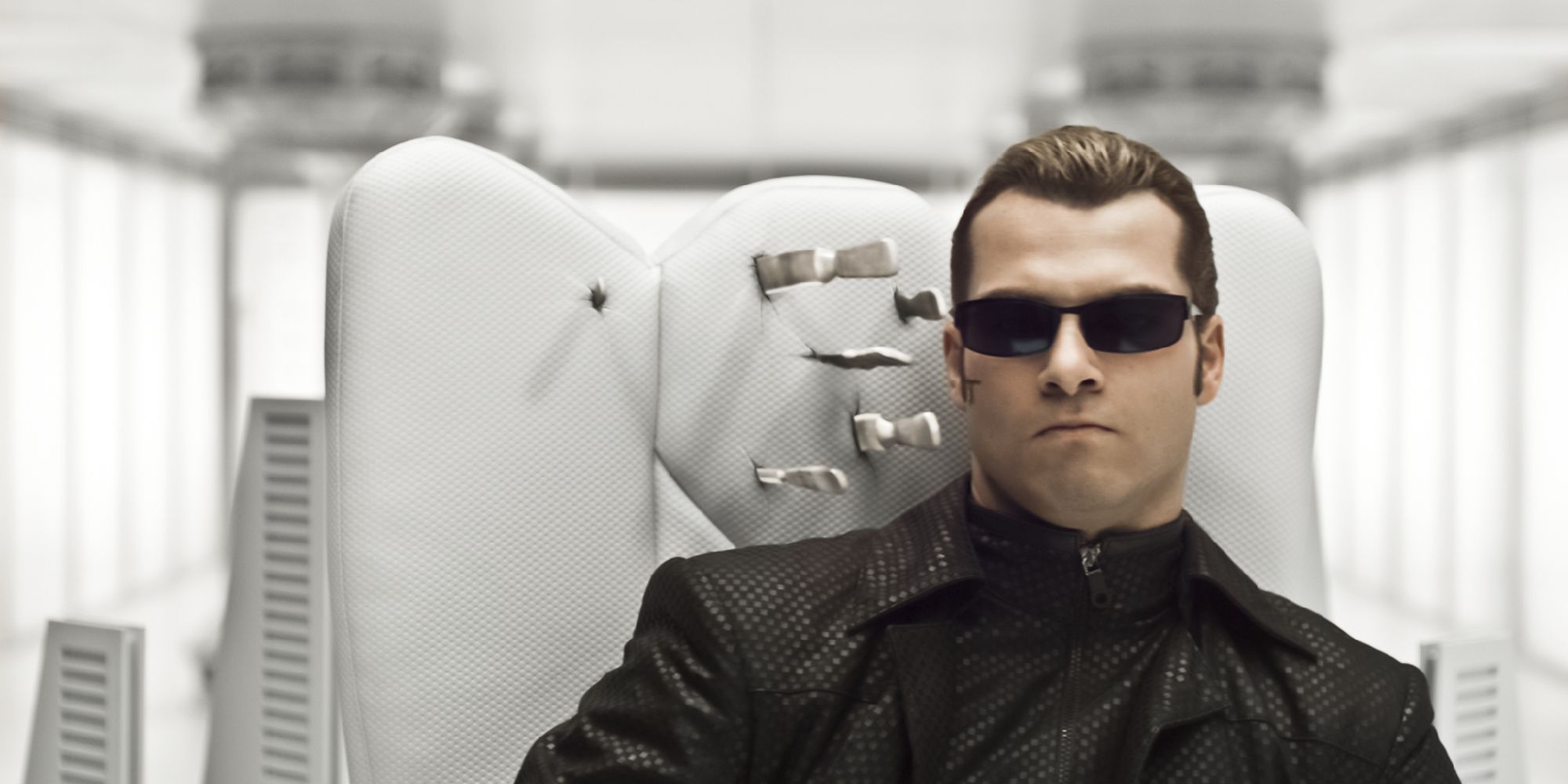 Wesker sat in a white chair in a clinically white room, the back of the chair next to his head skewered by several combat knives.