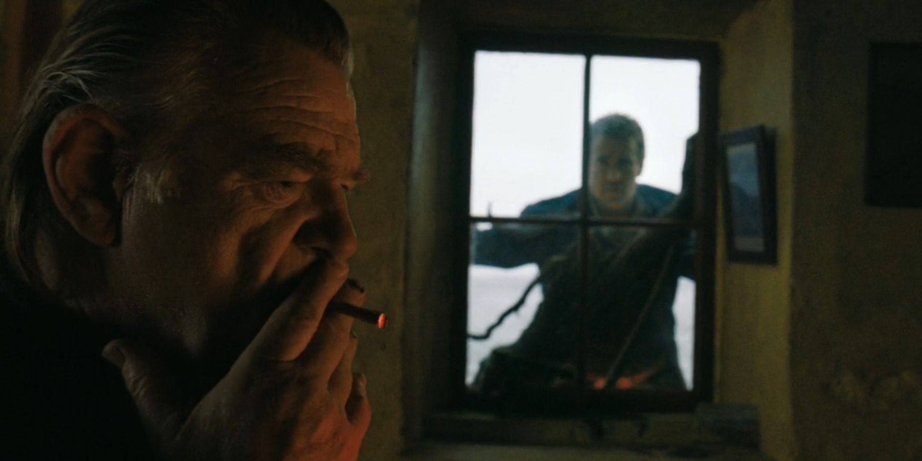 Brendan Gleeson smoking as Colm while Colin Farrell stares from window as Pádraic in The Banshees of Inisherin