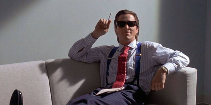 Christian Bale as Patrick Bateman sitting on office couch in American Psycho