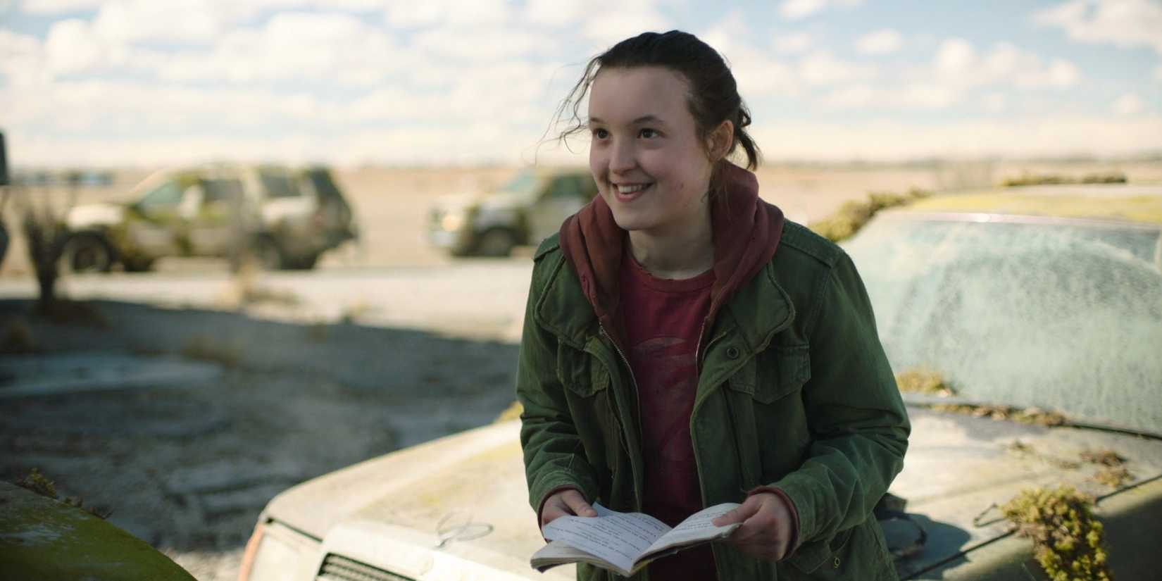 Bella Ramsey as Ellie smiling with pun book in HBO's The Last of Us