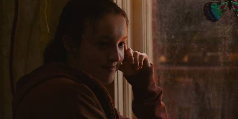 Ellie sitting by a widow in The Last of Us.