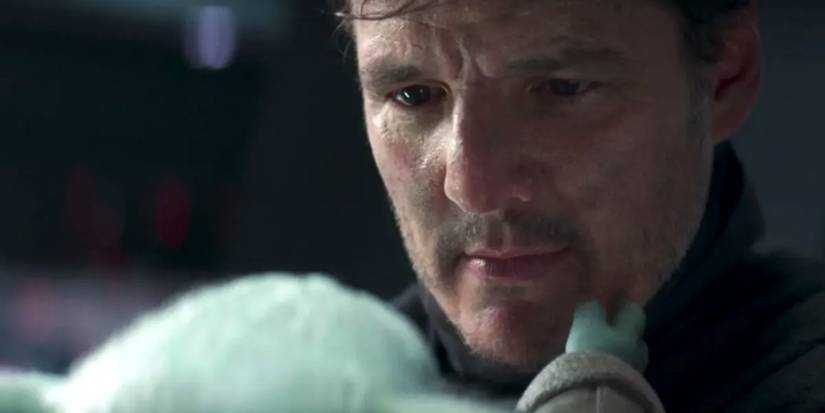 Pedro Pascal without helmet holding Grogu in The Mandalorian