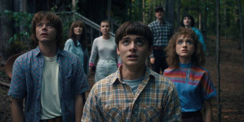 Ensemble cast of Stranger Things look up fearfully at the sky
