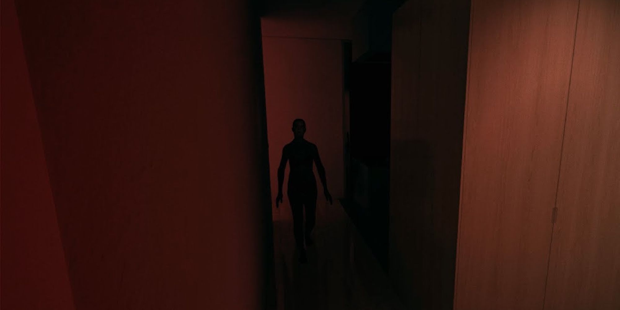 In the red corridor, a figure looms menacingly towards the viewer.