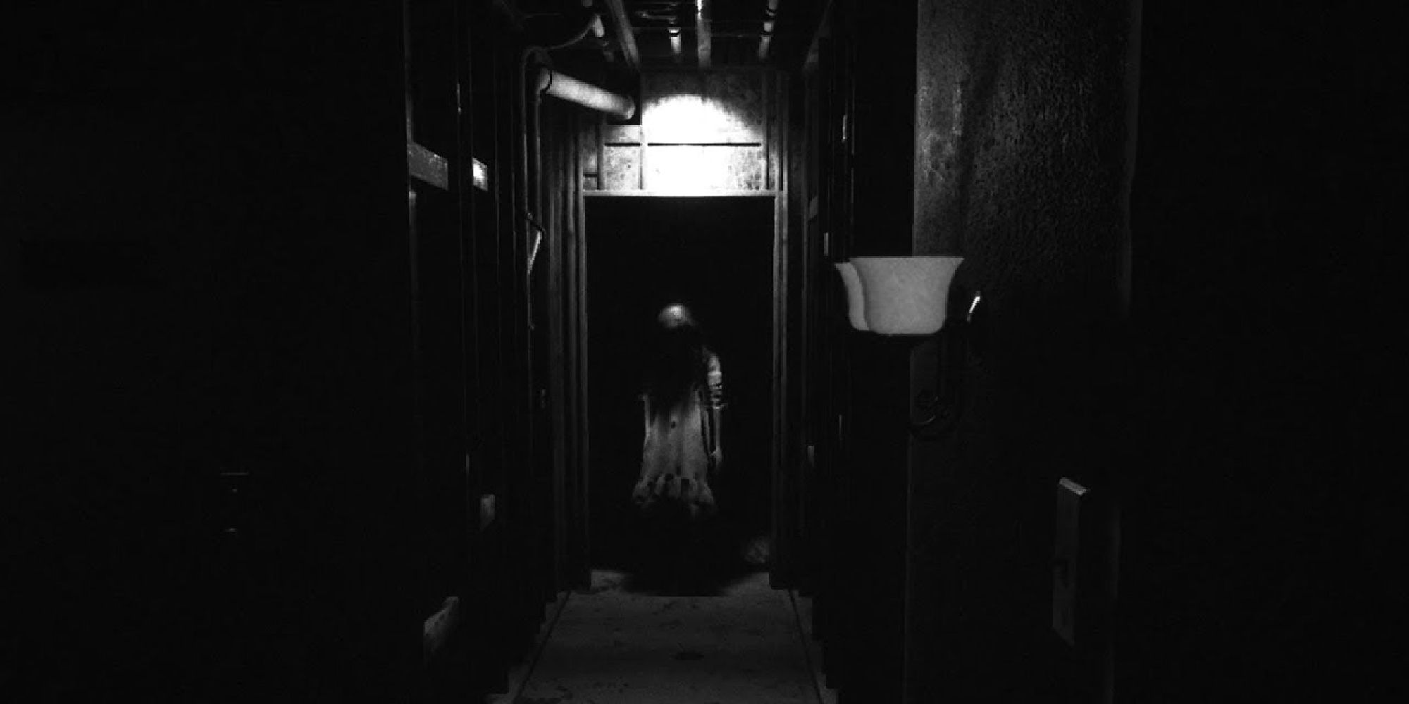 The ghost of a girl standing in a dark doorway at the end of a monochrome corridor. 