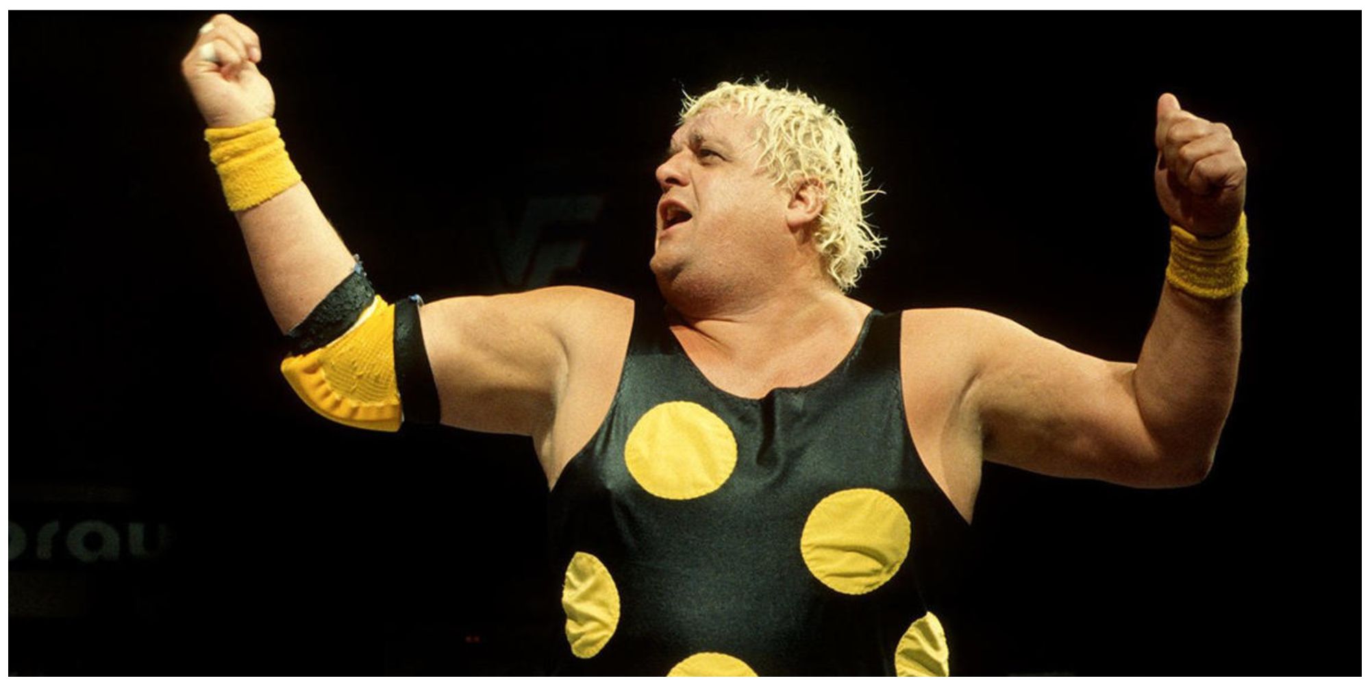 Dusty Rhodes in his polka-dot suit addressing the crowd with his arms in the air
