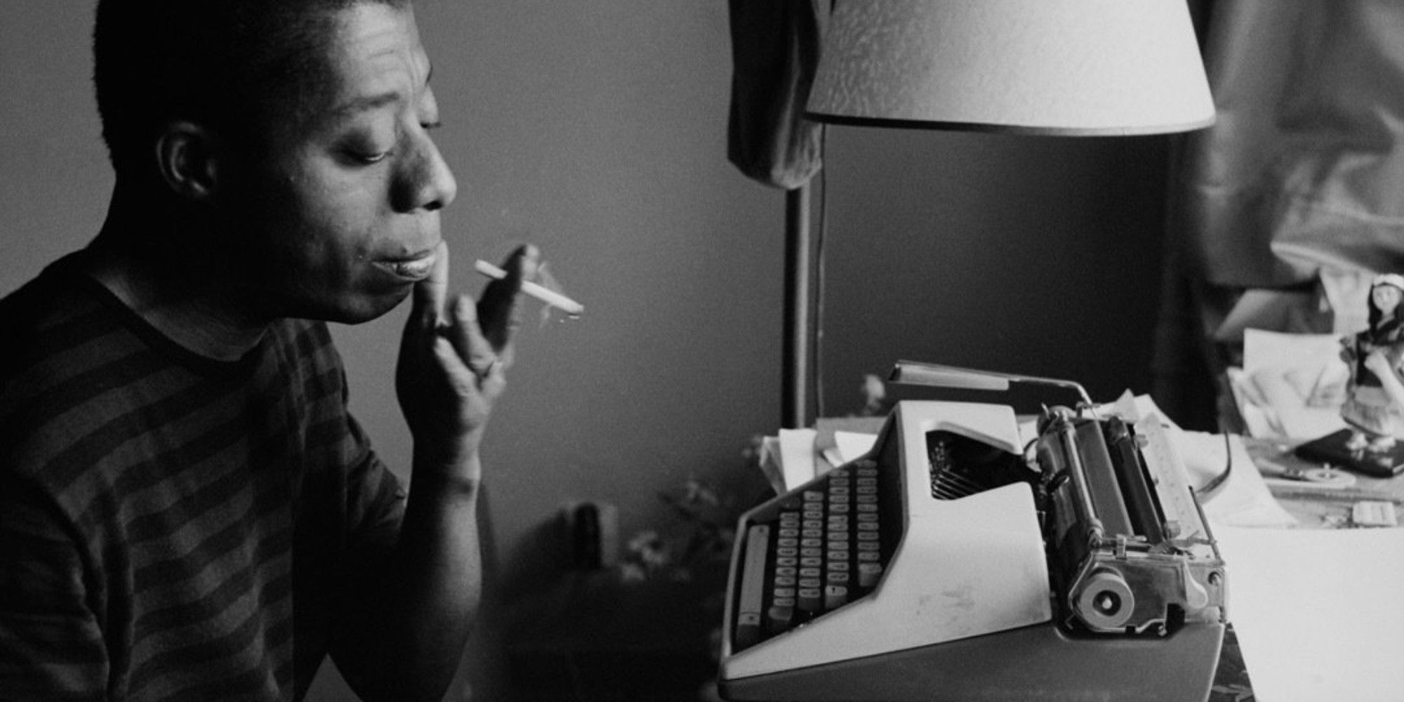 (Photo) black and white photo of a black man smoking a cigarette in front of a typewriter