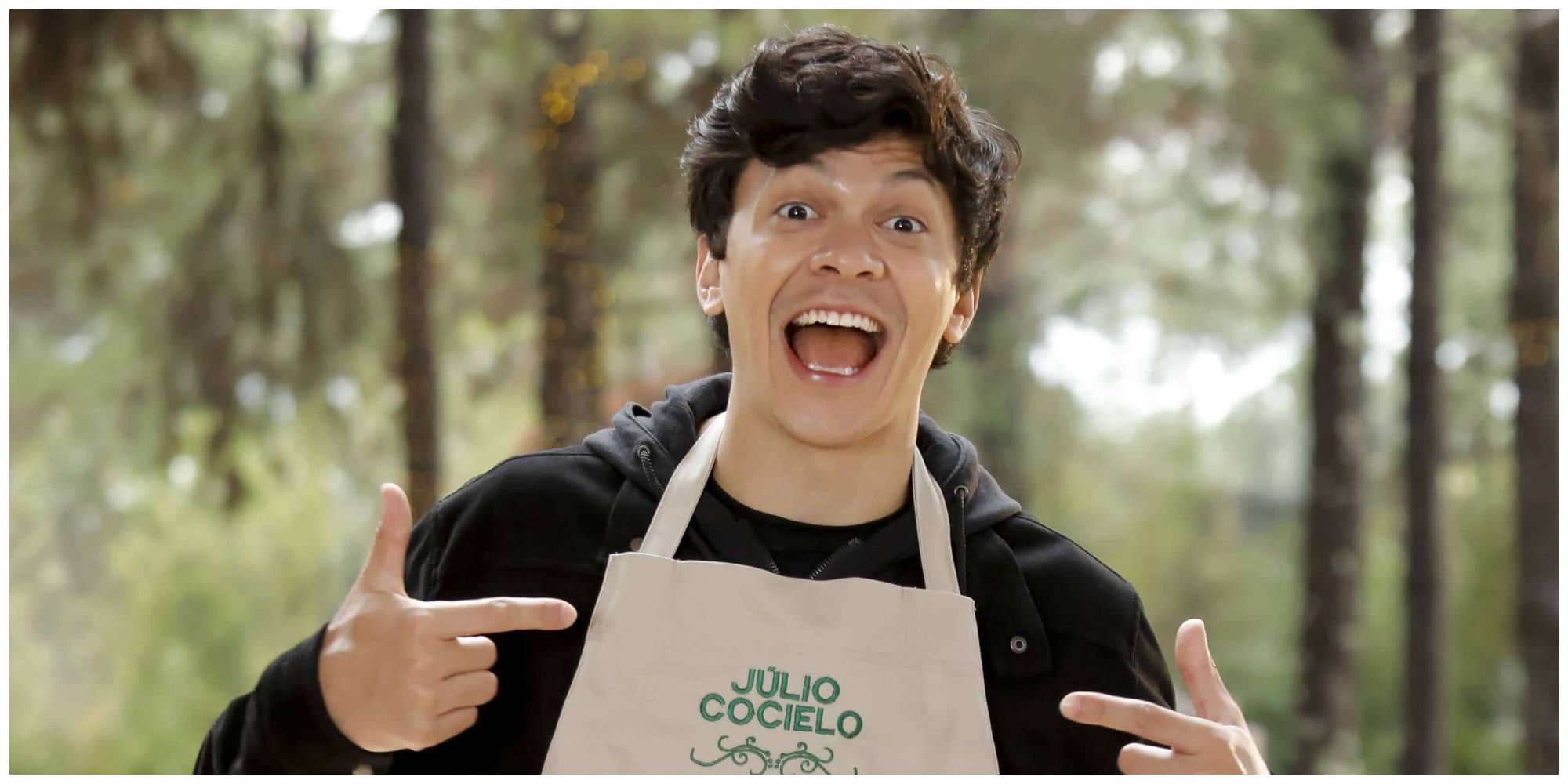 Julio Cocielo smiling and pointing to the apron he is wearing, which has his name on it.