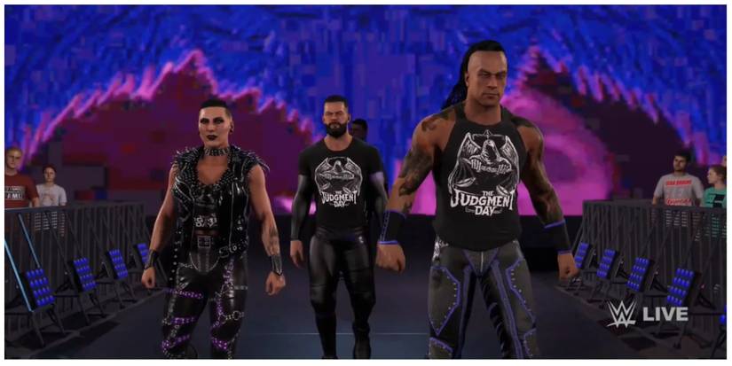 Rhea Ripley, Finn Balor and Damien Priest of the Judgment Day walking to the ring. In the background is a screen with dark blue/purple angel wings.