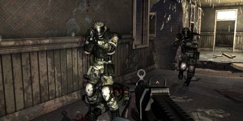 Screenshot of the FEAR protagonist leveling his gun at enemies from a first-person perspective in a run-down building