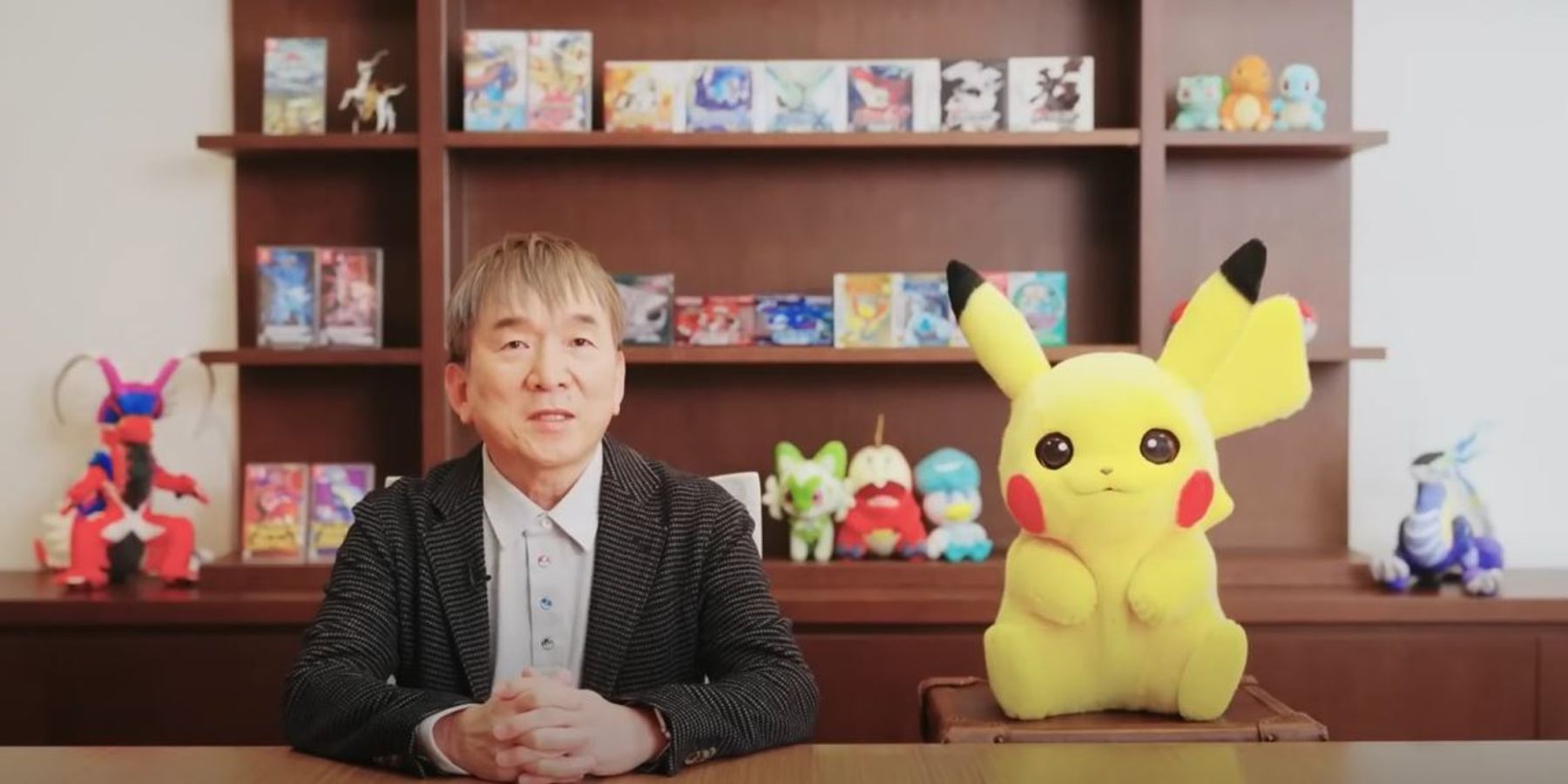 An image of Tsunekazu Ishihara and Pikachu sitting at a desk.