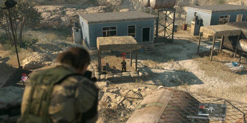 Snake looking down the sights of a gun at a guard who appears to be guarding an enemy force's base in METAL GEAR SOLID V: THE PHANTOM PAIN 
